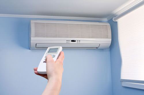 Homeowner using remote to control ductless mini-split wall unit