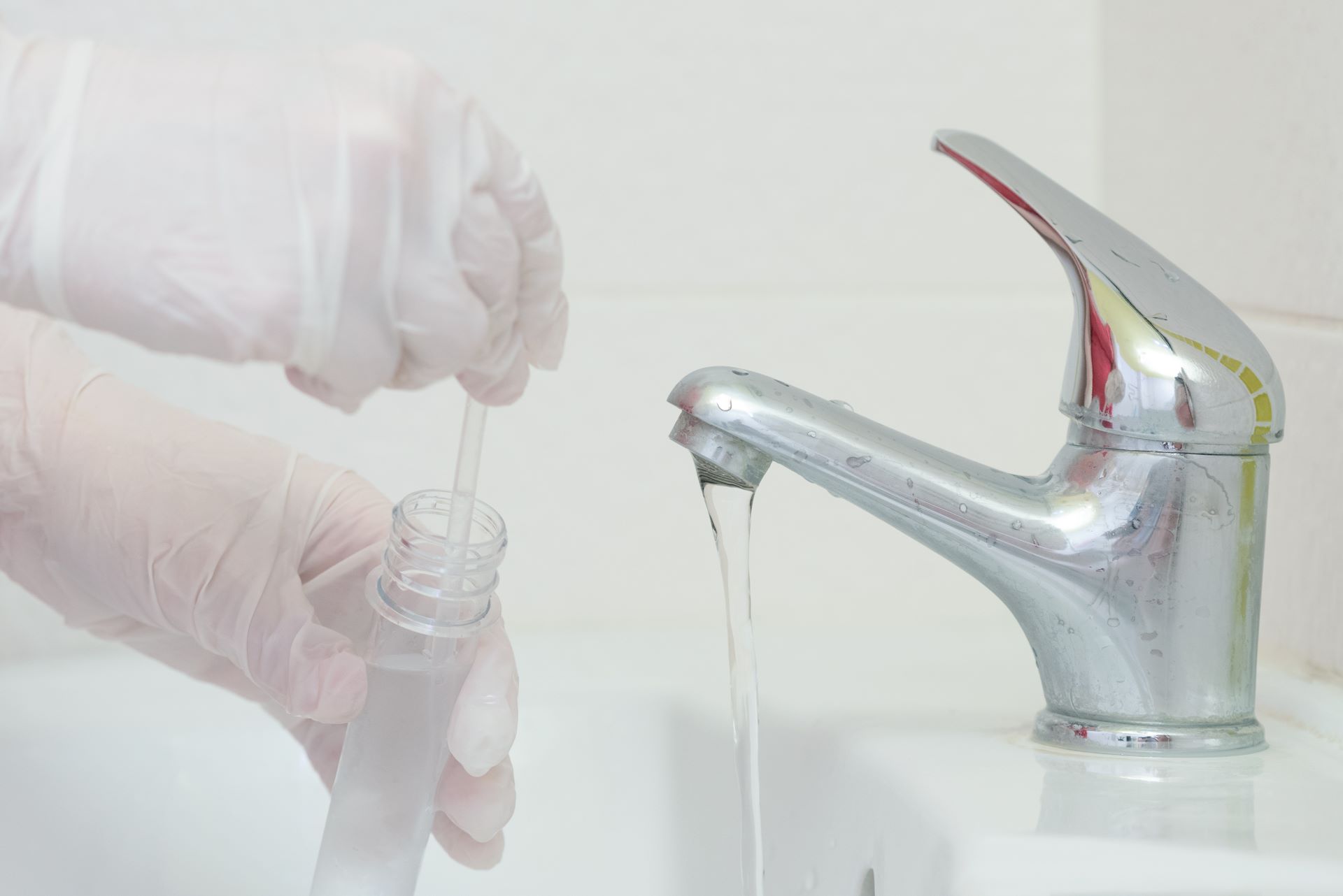 Closeup of someone testing water coming out of a faucet, using a test tube.